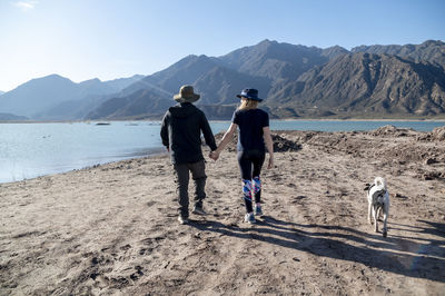 Couple holding hands while walking outdoors with natural landscape of mountains and lake.