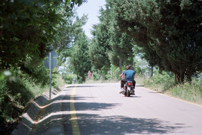 Rear view of men riding motorcycle on road