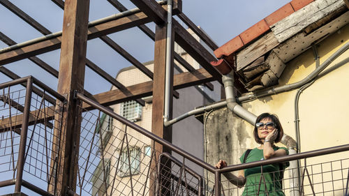 Portrait of young woman standing on railing against sky