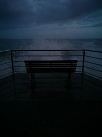 Empty bench by sea against sky