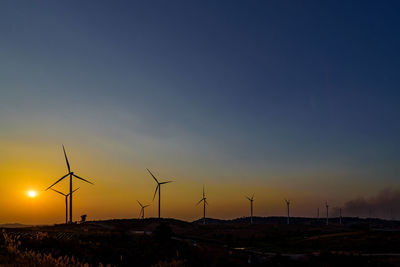 Wind turbines on land against sky during sunset