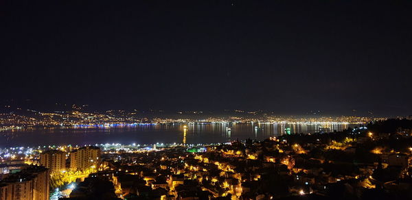 High angle view of illuminated city by sea against sky