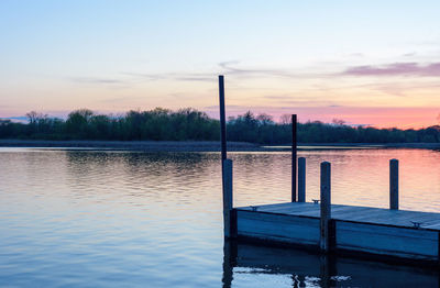 Wooden post in lake against sky during sunset