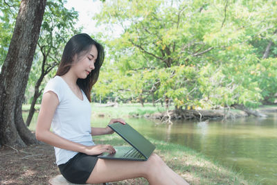 Young woman sitting by tree trunk against lake