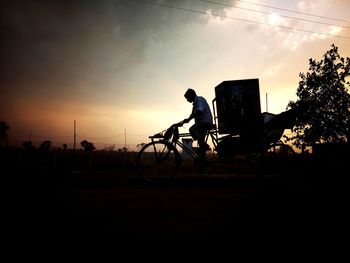 Silhouette man with bicycle on field against sky during sunset
