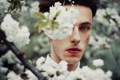 Close-up portrait of serious young man with white flowers in foreground