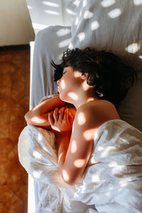 Child with dark hair sleeping on side in parents bed in the morning light