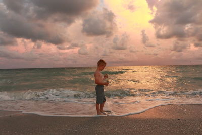 Rear view of shirtless boy standing on beach against sky