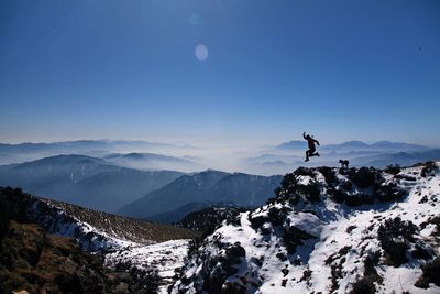 Silhouette man jumping on mountain against clear blue sky during sunny day