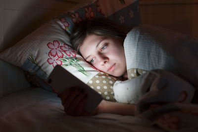 Sleepy tired girl lying in bed using smartphone at late night, can not sleep. social media addiction