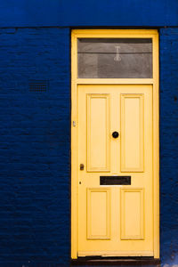 Closed wooden door painted in yellow on traditional brick facade painted in blue in london