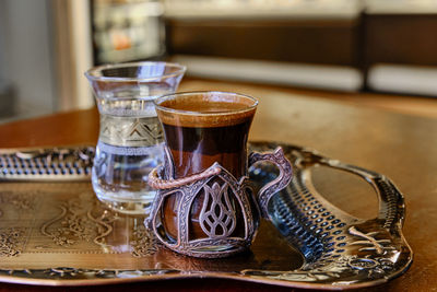 Turkish coffee with froth in a beautiful small glass and a glass of clean water on a tray in a cafe.