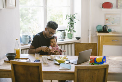 Father and daughter sitting on table at home