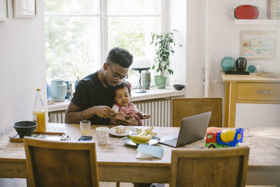 Young man playing with daughter while sitting at table in house