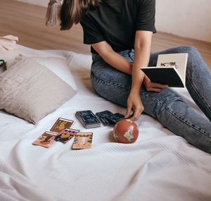 Midsection of woman with tarot cards on bed at home