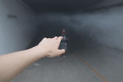 Cropped hand gesturing against male friend walking in tunnel