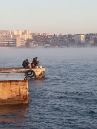 People in sea by buildings against sky in city