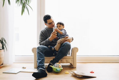 Full length of father playing with toddler son while sitting on sofa at home