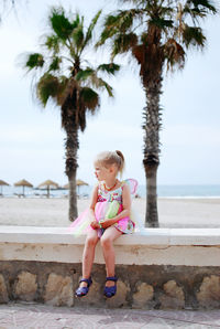 Full length of cute little girl in butterfly costume sitting on beach