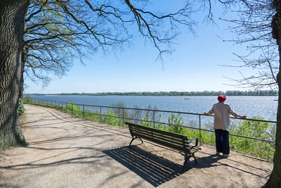 Man on railing by lake against sky