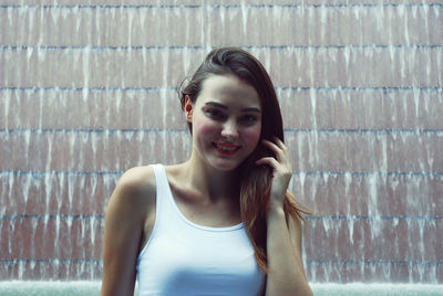Portrait of smiling young woman against artificial waterfall