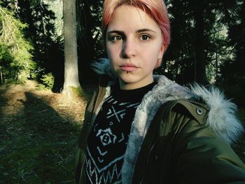 Close-up portrait of young woman standing against tree trunk