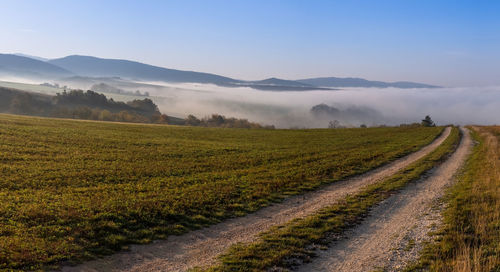 Dirt road amidst field against sky