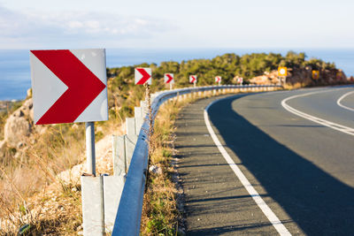 Road leading towards sign against sky