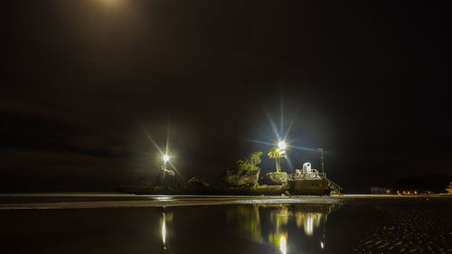 Illuminated lights by sea against sky at night