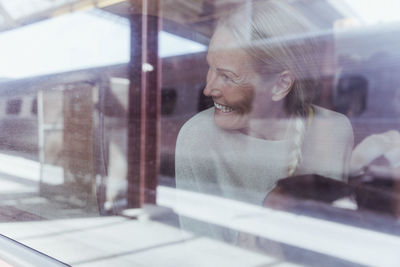 Smiling mature woman looking through window while traveling in train