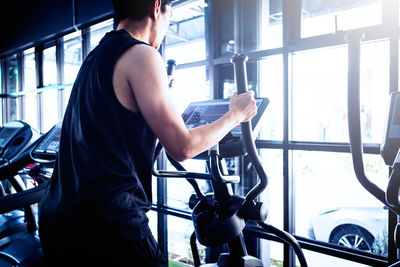 Rear view of man holding bicycle against window