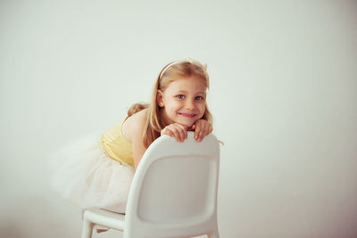 Portrait of cute smiling girl sitting on chair against wall