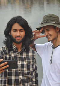 Two male friends having fun while taking selfie together in beside of lake