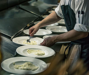 Midsection of chef serving food in plate