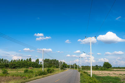 Road by electricity pylons against sky