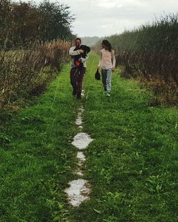 Friends with dog walking on grassy field during rainy season