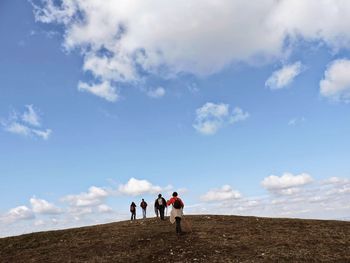 Low angle view of friends hiking on mountain against blue sky