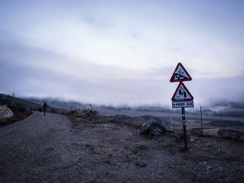 Road sign on field against sky