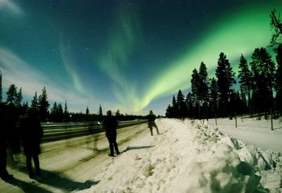 Blurred motion people on snow covered road against aurora borealis