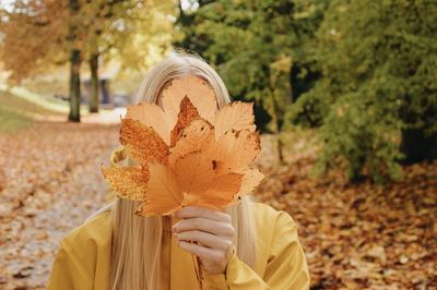 Portrait of person hiding behind autumn leaves, holding leaves in front of face