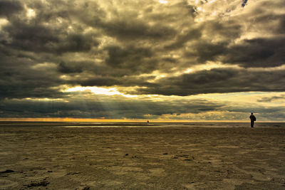 Silhouette man standing on beach against dramatic sky