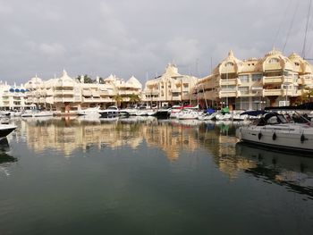 Sailboats moored in harbor by buildings against sky