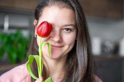 Close-up portrait of young woman holding red flower