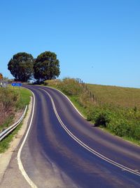 Road passing through landscape against clear blue sky