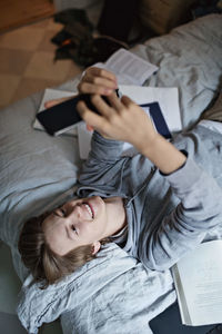 High angle view of smiling teenage boy using mobile phone while studying in bedroom