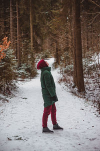 A girl in warm clothes stands and looks at the forest. winter sports walk alone in nature