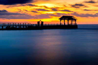 Silhouette pier over sea against sky during sunset