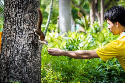 Side view of young man against tree trunk