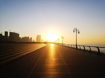 Empty footpath by lake against sky during sunset