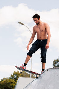 Low section of man skateboarding on field against sky